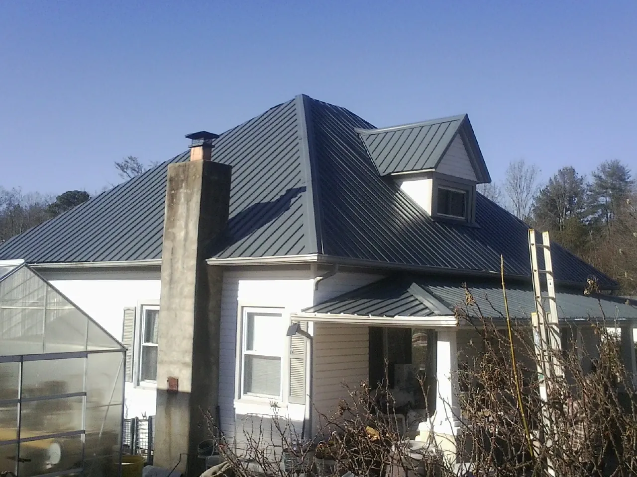 Dark blue standing seam metal roof on a white farmhouse with dormer — Slate & Tile Roof Repair by Roofing Brothers in Albertson