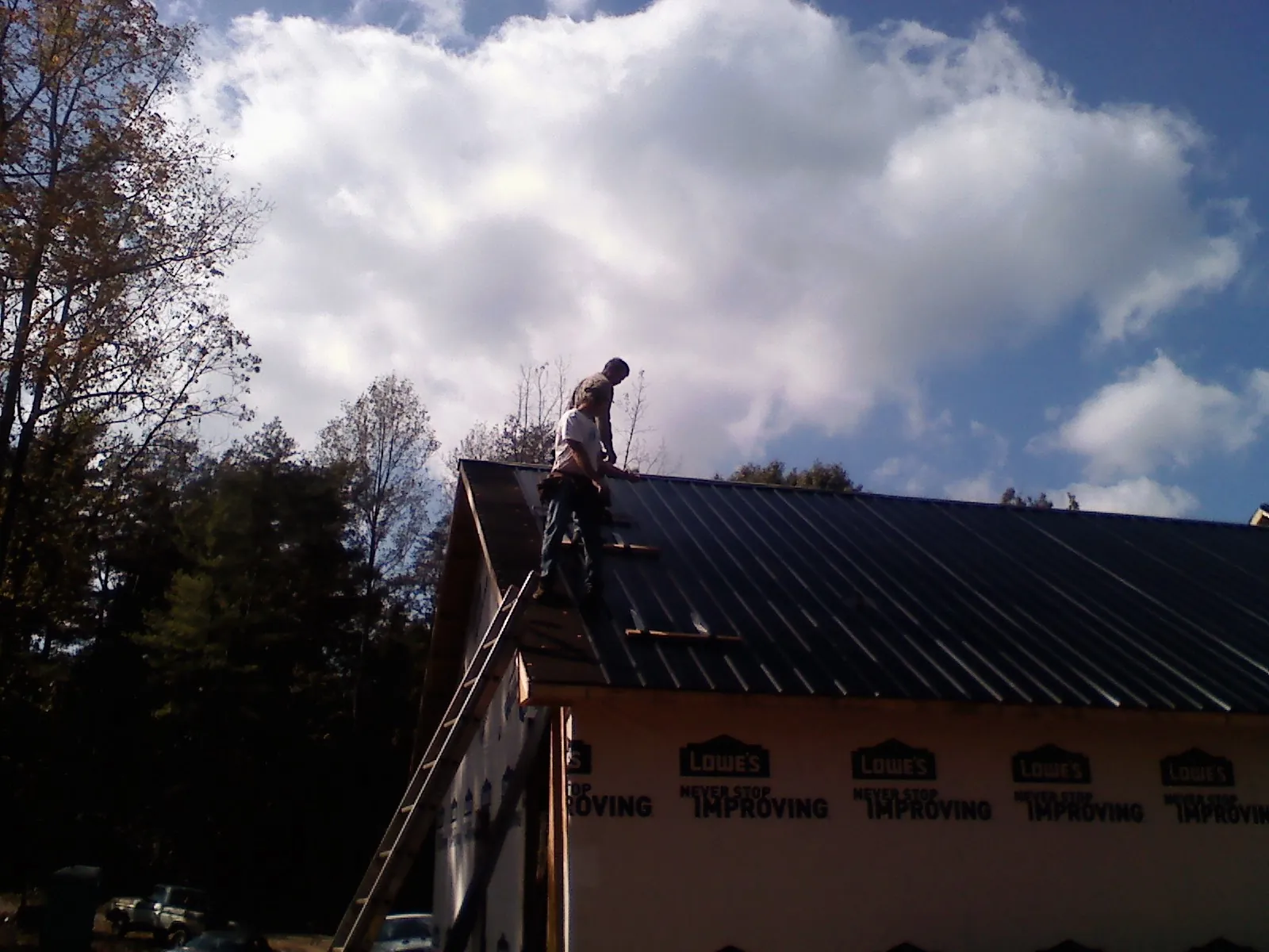 Roofer fastening dark metal panels high against a cloudy sky, from a Roof Inspection job in Albertson