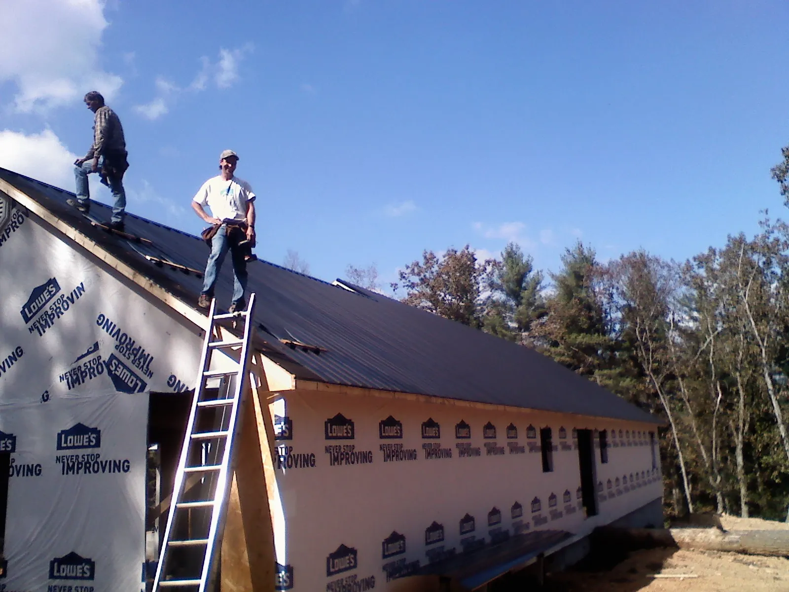 Two roofers standing on a long dark metal roof over a wrapped building in Albertson